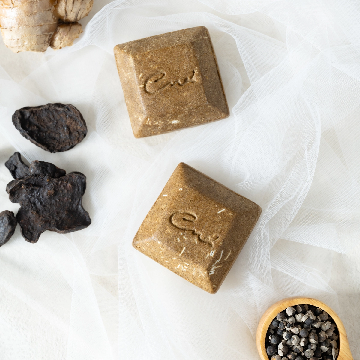Square handmade soap bars with an imprinted surface pattern resting on fabric