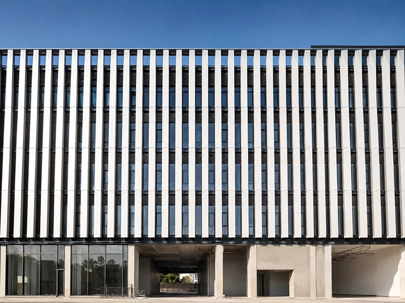 White vertical aluminum sunshade fins across a dark glazed facade