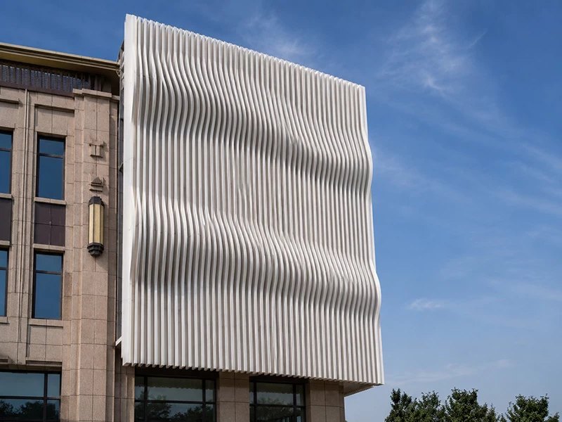 White wavy vertical aluminum fins forming a sculptural building screen