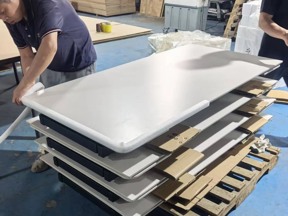 Workers fitting protective foam around white tabletops stacked for handling
